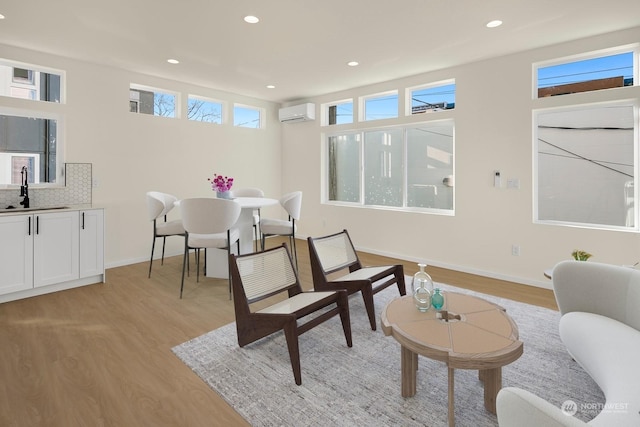 living area featuring sink, a wall unit AC, and light wood-type flooring