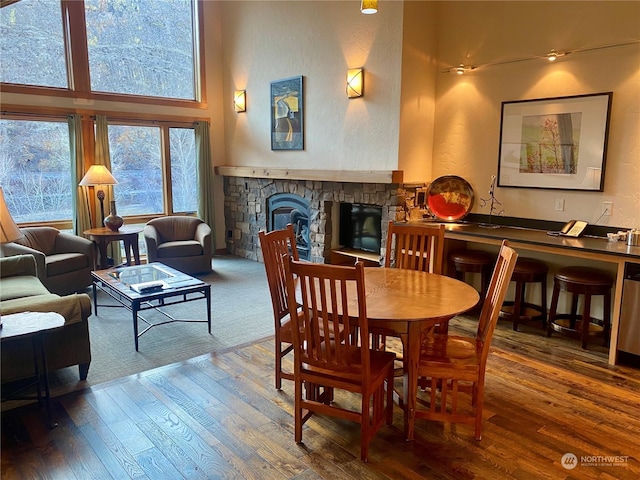 dining area with a stone fireplace, a high ceiling, and hardwood / wood-style flooring