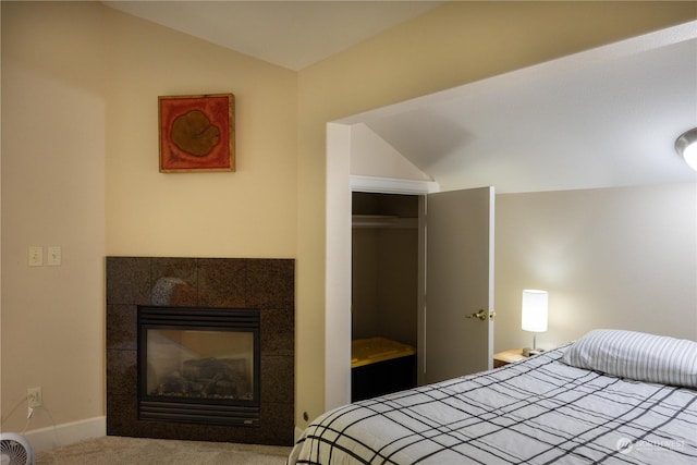 bedroom with a tiled fireplace, lofted ceiling, and carpet