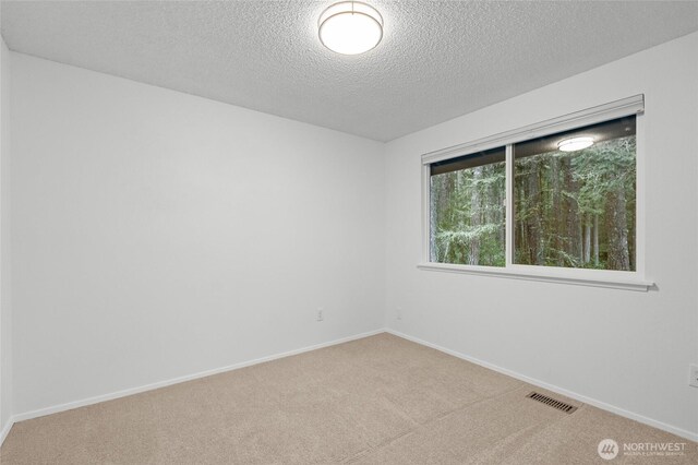 unfurnished room with light carpet, baseboards, visible vents, and a textured ceiling