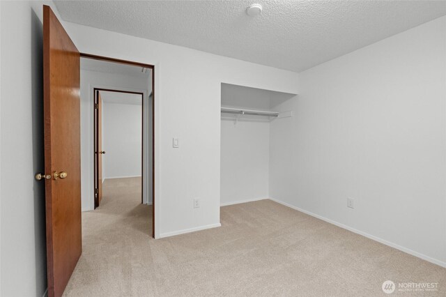 unfurnished bedroom with a closet, light carpet, a textured ceiling, and baseboards