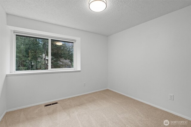 spare room featuring baseboards, a textured ceiling, visible vents, and carpet flooring