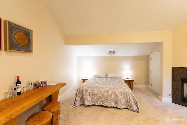 carpeted bedroom with lofted ceiling and a tiled fireplace