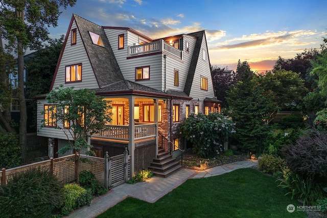 back house at dusk with a balcony and a lawn