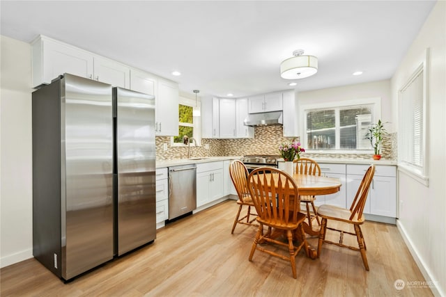 kitchen with pendant lighting, appliances with stainless steel finishes, white cabinetry, backsplash, and light hardwood / wood-style floors