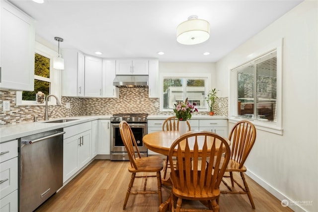 kitchen with appliances with stainless steel finishes, pendant lighting, sink, white cabinets, and wall chimney exhaust hood