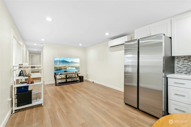 kitchen with stainless steel refrigerator, tasteful backsplash, a wall mounted air conditioner, white cabinets, and light wood-type flooring