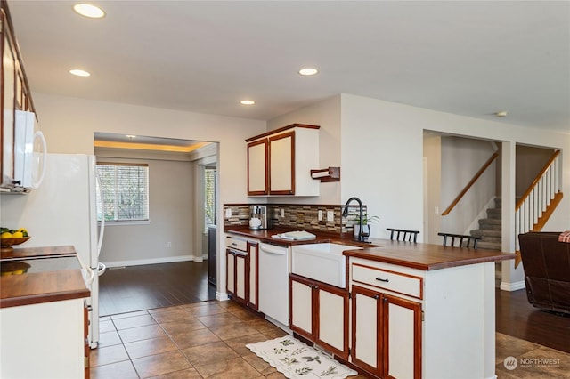 kitchen with sink, dark tile patterned flooring, decorative backsplash, kitchen peninsula, and white appliances