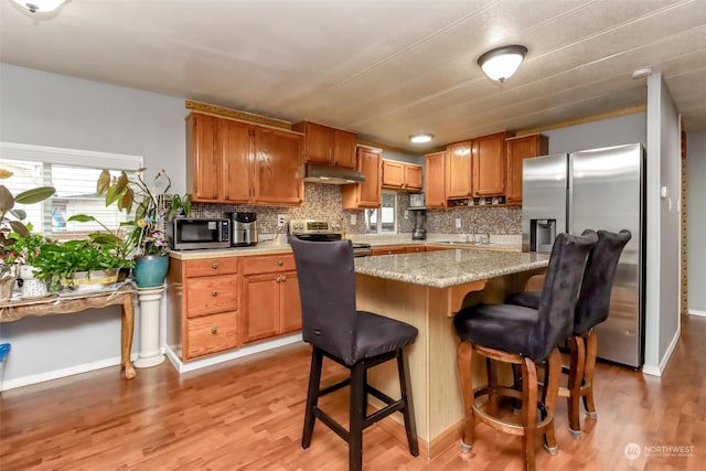 kitchen featuring tasteful backsplash, stainless steel appliances, a kitchen breakfast bar, and light hardwood / wood-style floors