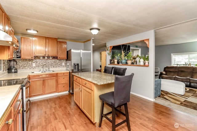 kitchen with appliances with stainless steel finishes, a kitchen breakfast bar, sink, and light hardwood / wood-style flooring