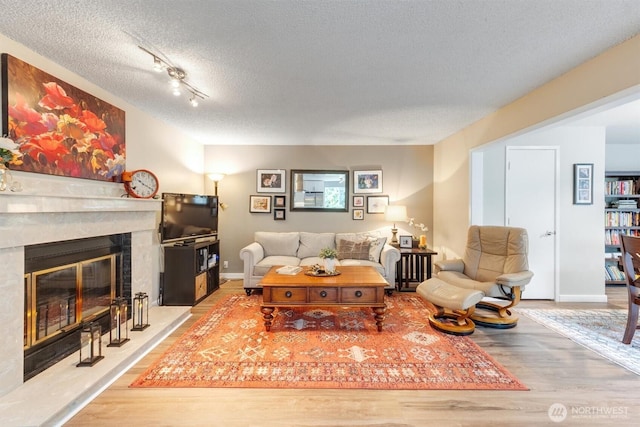 living room with baseboards, a textured ceiling, wood finished floors, and a fireplace