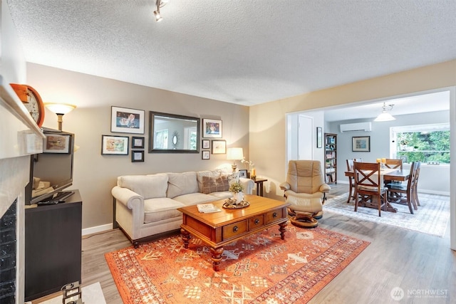 living area featuring a wall unit AC, light wood-style flooring, baseboards, and a textured ceiling