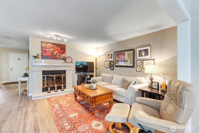 living room featuring track lighting, a textured ceiling, wood finished floors, a fireplace, and baseboards