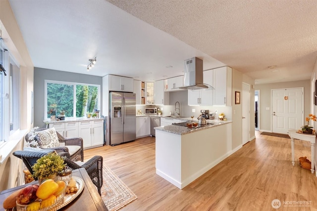 kitchen with a peninsula, stainless steel appliances, light wood-style floors, white cabinetry, and exhaust hood