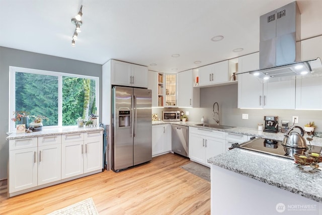 kitchen featuring appliances with stainless steel finishes, light wood-style floors, island range hood, white cabinets, and a sink