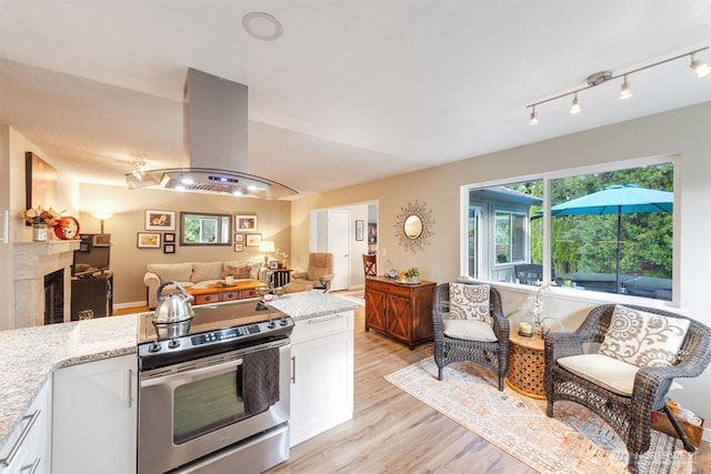 kitchen featuring open floor plan, a tile fireplace, stainless steel electric range, island exhaust hood, and white cabinetry