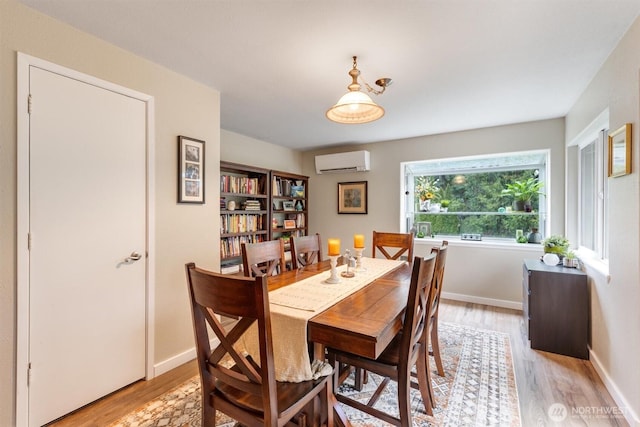 dining area with baseboards, an AC wall unit, and light wood-style floors