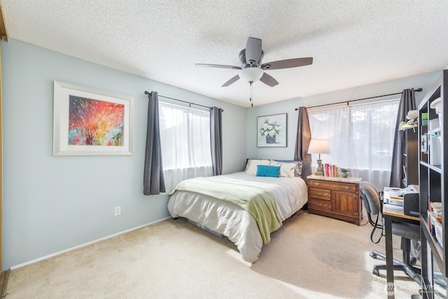 bedroom featuring a textured ceiling, light colored carpet, baseboards, and ceiling fan