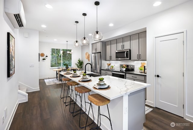 kitchen featuring hanging light fixtures, an AC wall unit, gray cabinets, an island with sink, and stainless steel appliances