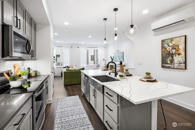 kitchen featuring a wall mounted AC, stainless steel appliances, gray cabinets, and a kitchen island with sink