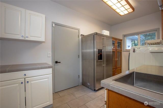 kitchen featuring stainless steel refrigerator with ice dispenser, white cabinetry, light tile patterned flooring, and tile counters