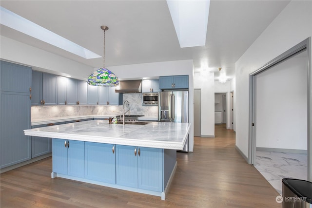 kitchen featuring blue cabinetry, decorative light fixtures, a skylight, a center island with sink, and stainless steel appliances