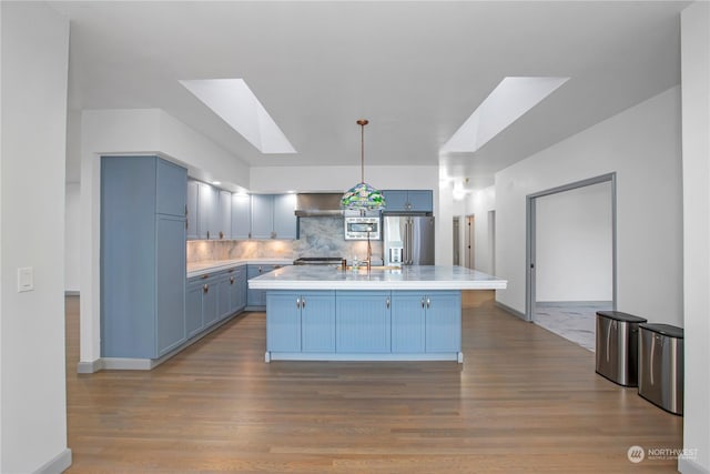 kitchen with appliances with stainless steel finishes, a skylight, a center island, blue cabinets, and decorative light fixtures