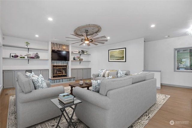 living room with a fireplace, ceiling fan, and light wood-type flooring