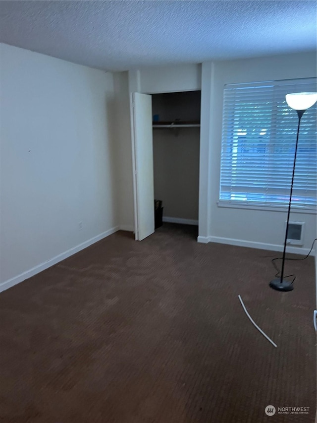 unfurnished bedroom with a closet, a textured ceiling, and dark colored carpet