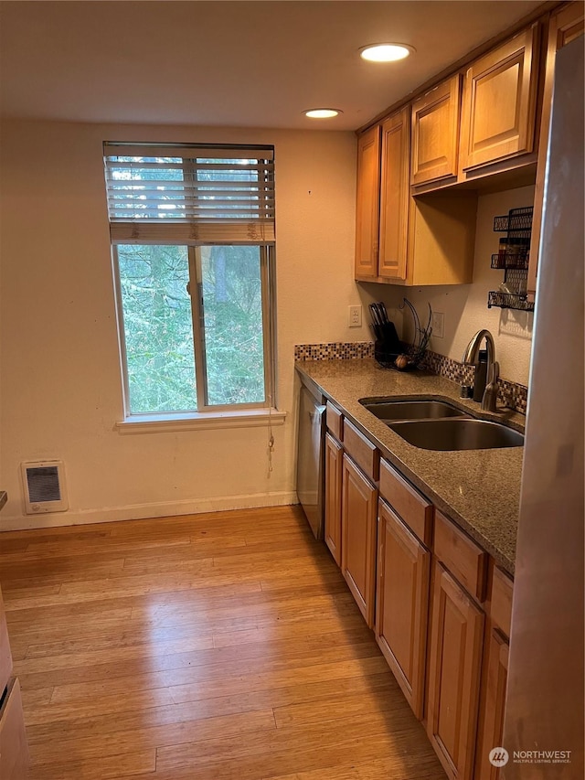 kitchen with sink, heating unit, light wood-type flooring, dishwasher, and stone counters