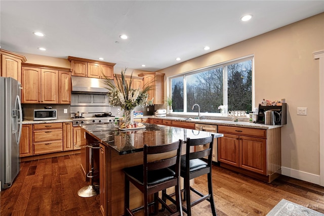 kitchen featuring a breakfast bar area, a center island, dark stone countertops, appliances with stainless steel finishes, and dark hardwood / wood-style floors