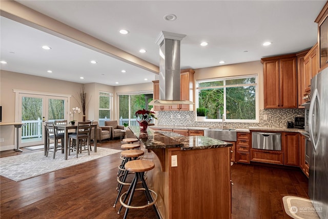 kitchen featuring a kitchen island, island range hood, a breakfast bar area, dark hardwood / wood-style flooring, and dark stone counters