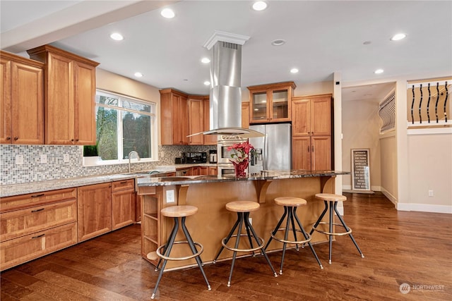 kitchen with stainless steel refrigerator with ice dispenser, island exhaust hood, a center island, and a kitchen bar