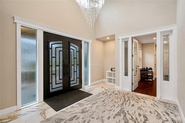 foyer entrance with a towering ceiling, a notable chandelier, and french doors