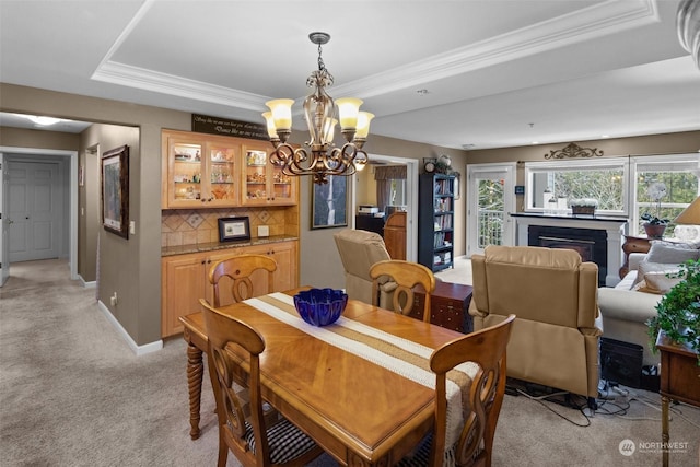 carpeted dining space featuring a tray ceiling, ornamental molding, and a chandelier