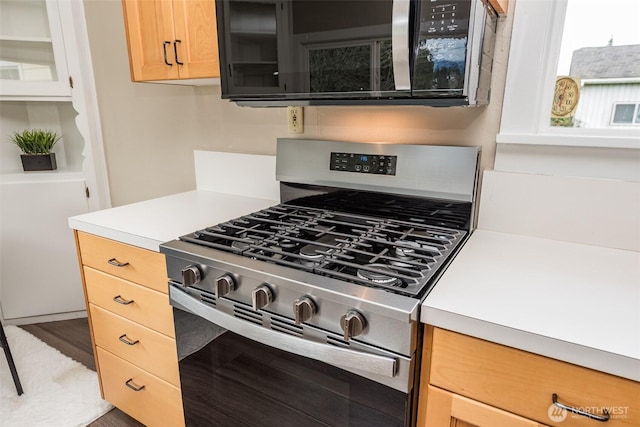 kitchen featuring light countertops, glass insert cabinets, light brown cabinetry, and stainless steel appliances