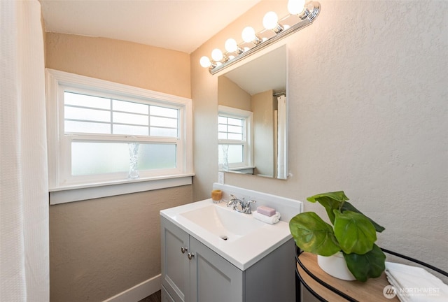 bathroom with vaulted ceiling, vanity, and a textured wall