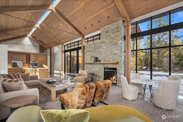 living room with wood ceiling, plenty of natural light, a stone fireplace, and beamed ceiling