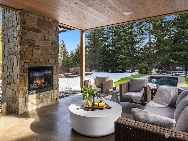 snow covered patio featuring an outdoor stone fireplace