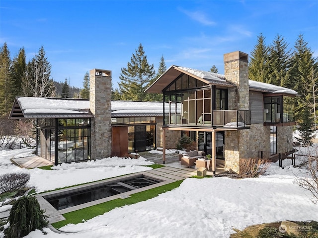 snow covered back of property featuring a sunroom and a balcony