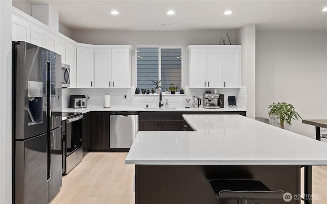 kitchen with tasteful backsplash, sink, white cabinets, stainless steel appliances, and light hardwood / wood-style flooring