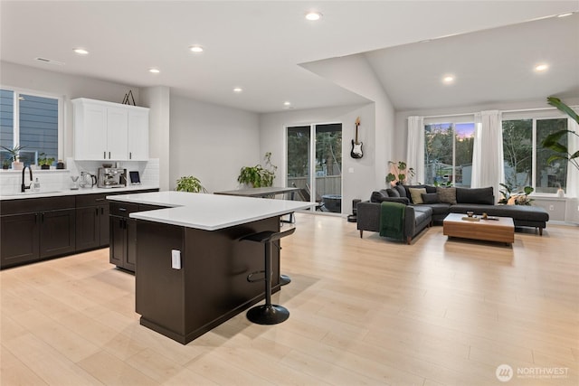 kitchen featuring sink, a breakfast bar area, a kitchen island, light hardwood / wood-style floors, and white cabinets