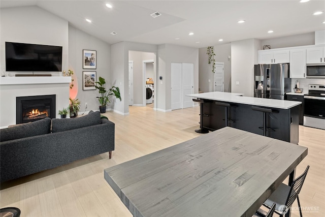 kitchen featuring a kitchen island, washer / clothes dryer, white cabinetry, stainless steel appliances, and light hardwood / wood-style flooring