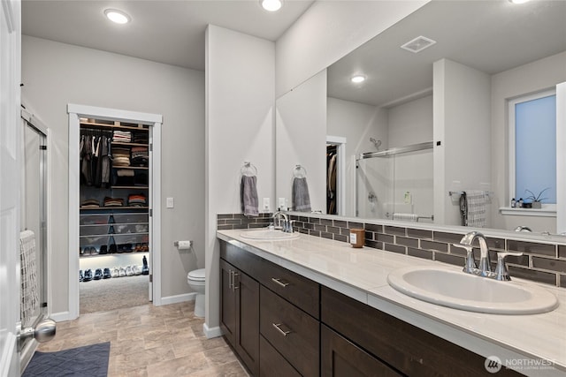 bathroom featuring vanity, toilet, a shower with shower door, and decorative backsplash