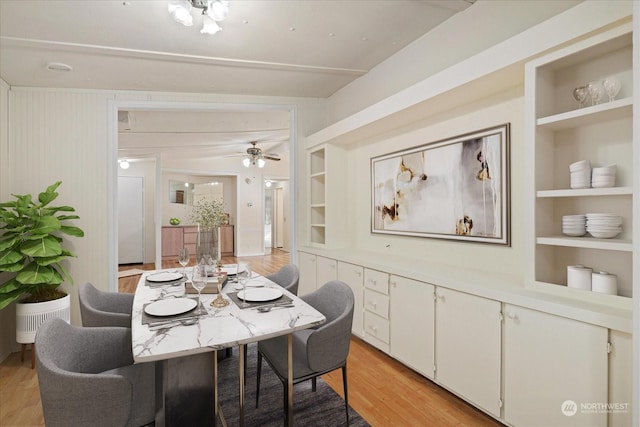 dining space with built in shelves, ceiling fan, and light wood-type flooring