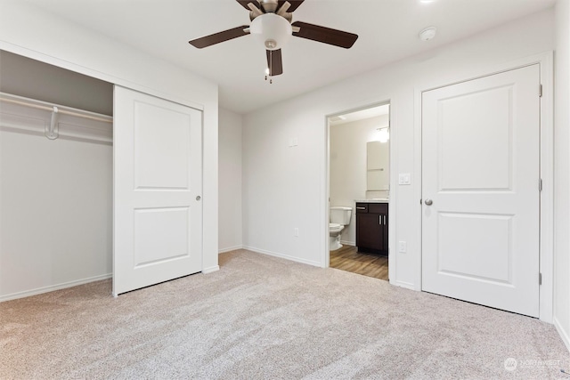 unfurnished bedroom featuring a closet, light colored carpet, ceiling fan, and ensuite bath