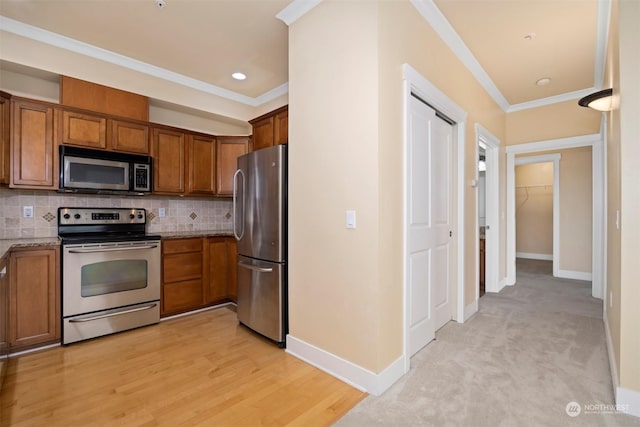 kitchen with backsplash, stainless steel appliances, light stone counters, ornamental molding, and light hardwood / wood-style floors