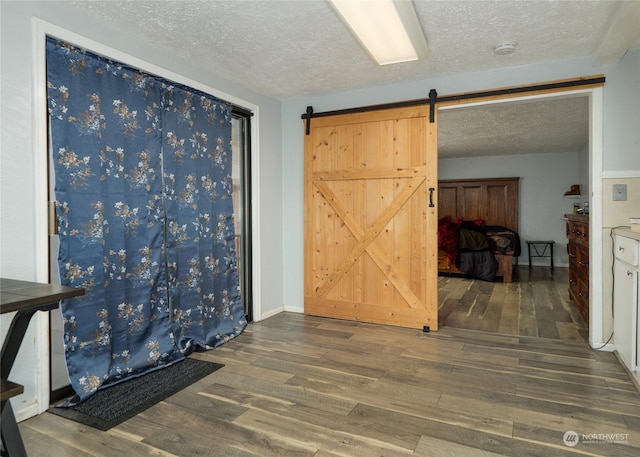 unfurnished room with dark wood-type flooring, a barn door, and a textured ceiling