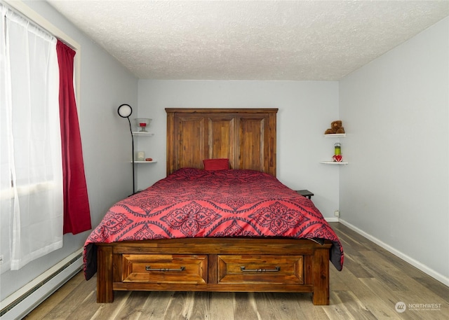 bedroom featuring a baseboard heating unit, hardwood / wood-style floors, and a textured ceiling