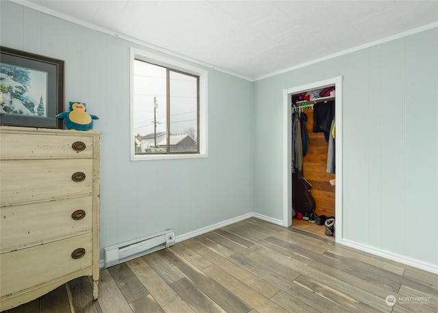 unfurnished bedroom with a baseboard heating unit, hardwood / wood-style flooring, a walk in closet, and a closet